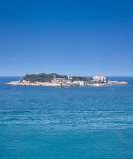 La pittoresque Île de Bendor, au large de Sanary-sur-Mer, avec ses bâtiments et sa végétation luxuriante, flottant sur les eaux bleues de la Méditerranée sous un ciel azur.