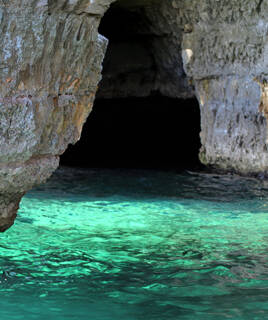 L'entrée du Gouffre de Padirac, près de Sarlat, révélant une ouverture sombre dans la roche avec des eaux souterraines aux teintes turquoise claires, offrant un aperçu de la grotte.
