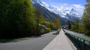 Promenade le long de la rivière Arve à Chamonix en Savoie, avec des bâtiments et des arbres, offrant une vue imprenable sur les sommets enneigés du massif du Mont Blanc en arrière-plan.