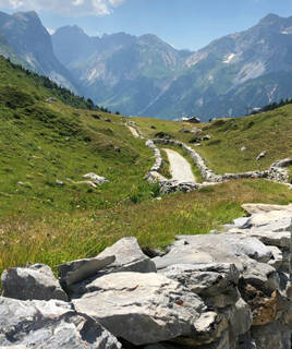 Un sentier de montagne pierreux serpentant à travers des prairies verdoyantes, avec des sommets rocheux en arrière-plan, dans le Parc National de la Vanoise en Savoie.