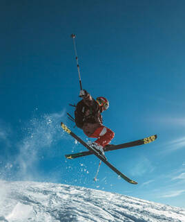 Un skieur réalisant un saut spectaculaire sur une piste enneigée en Savoie, avec le ciel bleu en arrière-plan, illustrant les sports d'hiver.