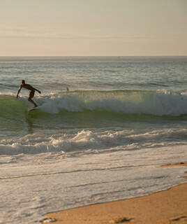 Un surfeur chevauchant une vague sur la plage de Seignosse, avec l'océan Atlantique s'étendant à l'horizon sous un ciel lumineux.