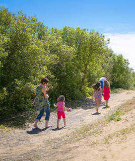 Une famille en randonnée sur un sentier en terre, bordé d'arbres et de végétation luxuriante, probablement près de La Seyne-sur-Mer, sous un ciel bleu ensoleillé.
