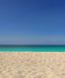 La plage de sable fin de Soulac-sur-Mer, bordée par les eaux turquoise de l'océan Atlantique sous un ciel d'un bleu profond et sans nuages.