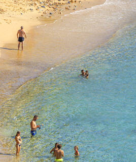 La plage du Mourillon à Toulon, avec ses eaux claires et son sable doré, où des baigneurs profitent de la mer sous le soleil.