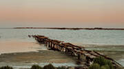 Un vieux ponton en bois partiellement immergé dans l'eau de l'Étang de Thau, près de Valras-Plage, s'étirant vers l'horizon sous un ciel aux teintes pastel du lever ou du coucher du soleil.