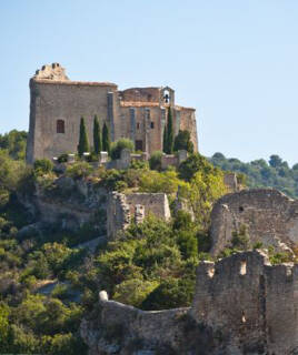 Les ruines du château de Saint-Saturnin-lès-Apt dans le Vaucluse, avec l'ancienne église et son clocher dominant les vestiges en pierre et la végétation méditerranéenne luxuriante, sous un ciel bleu clair.