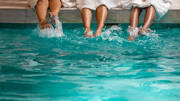 Pieds éclaboussant l'eau turquoise d'une piscine, probablement aux Thermes de Vittel, avec des personnes assises au bord.