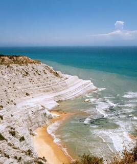 La Baia dei Turchi dans les Pouilles, une crique avec des falaises blanches escarpées, une petite plage de sable et des eaux turquoise, sous un ciel bleu clair.