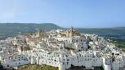 Le village blanc d'Ostuni dans les Pouilles, avec ses maisons blanchies à la chaux et ses églises dominantes, s'étageant à flanc de colline sous un ciel bleu clair.