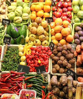 Un étal coloré d'un marché traditionnel basque à Capbreton, présentant une grande variété de fruits et légumes frais, comme des avocats, des piments rouges et verts, et d'autres produits locaux avec leurs prix affichés.