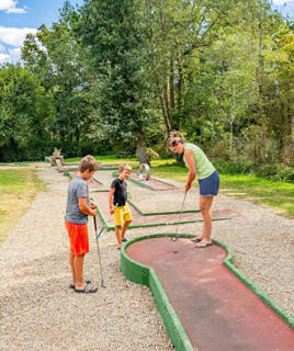Une famille avec deux enfants faisant une partie de mini-golf dans un camping