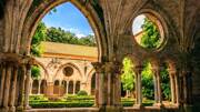 Arche de l'Abbaye de Fontfroide, avec des arbres autour ainsi qu'une vue sur le reste de l'Abbaye sous un ciel bleu